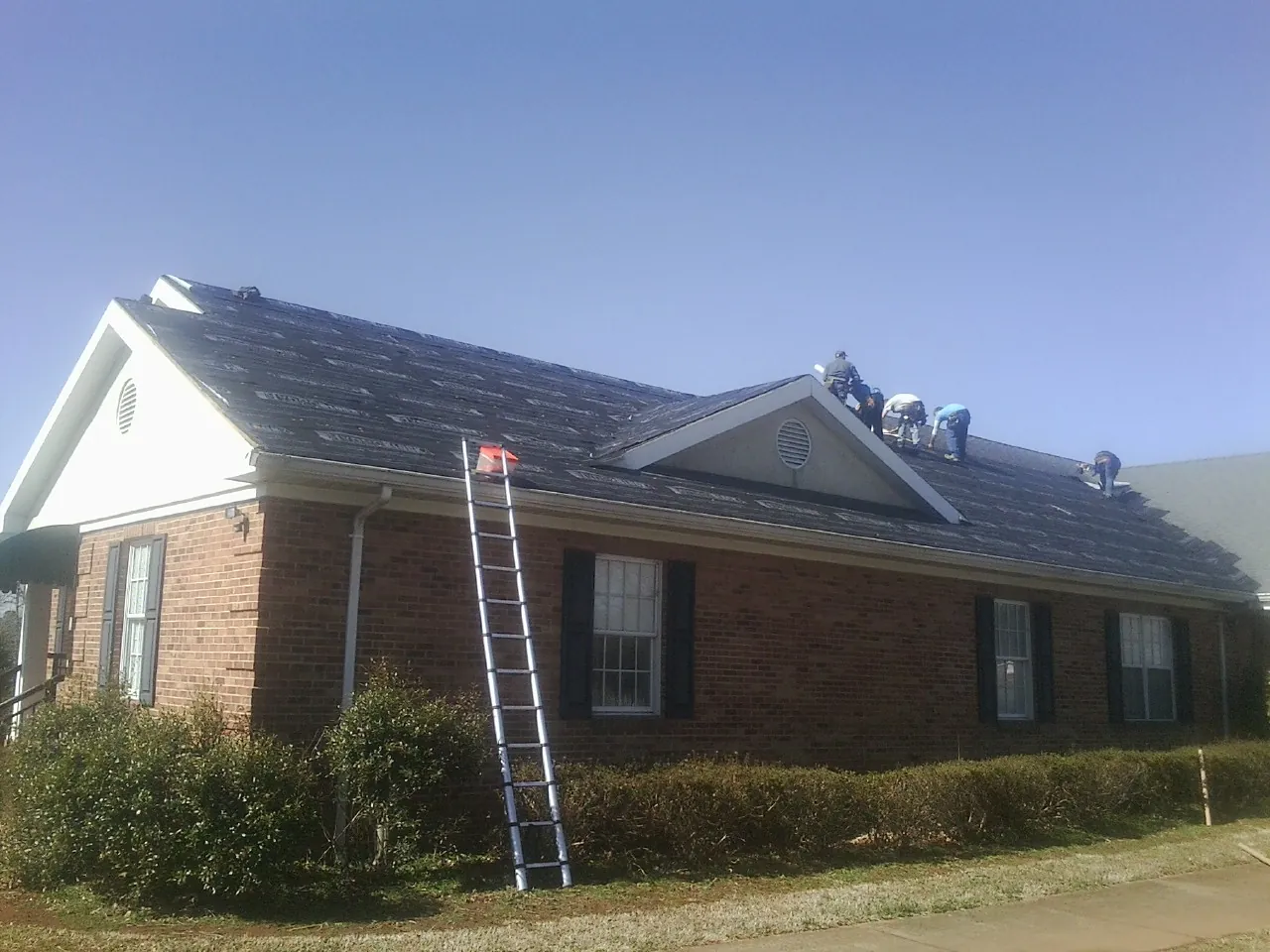 Crew tearing shingles off a brick ranch roof with a ladder set — Metal Roof Repair work by our crew in Walland