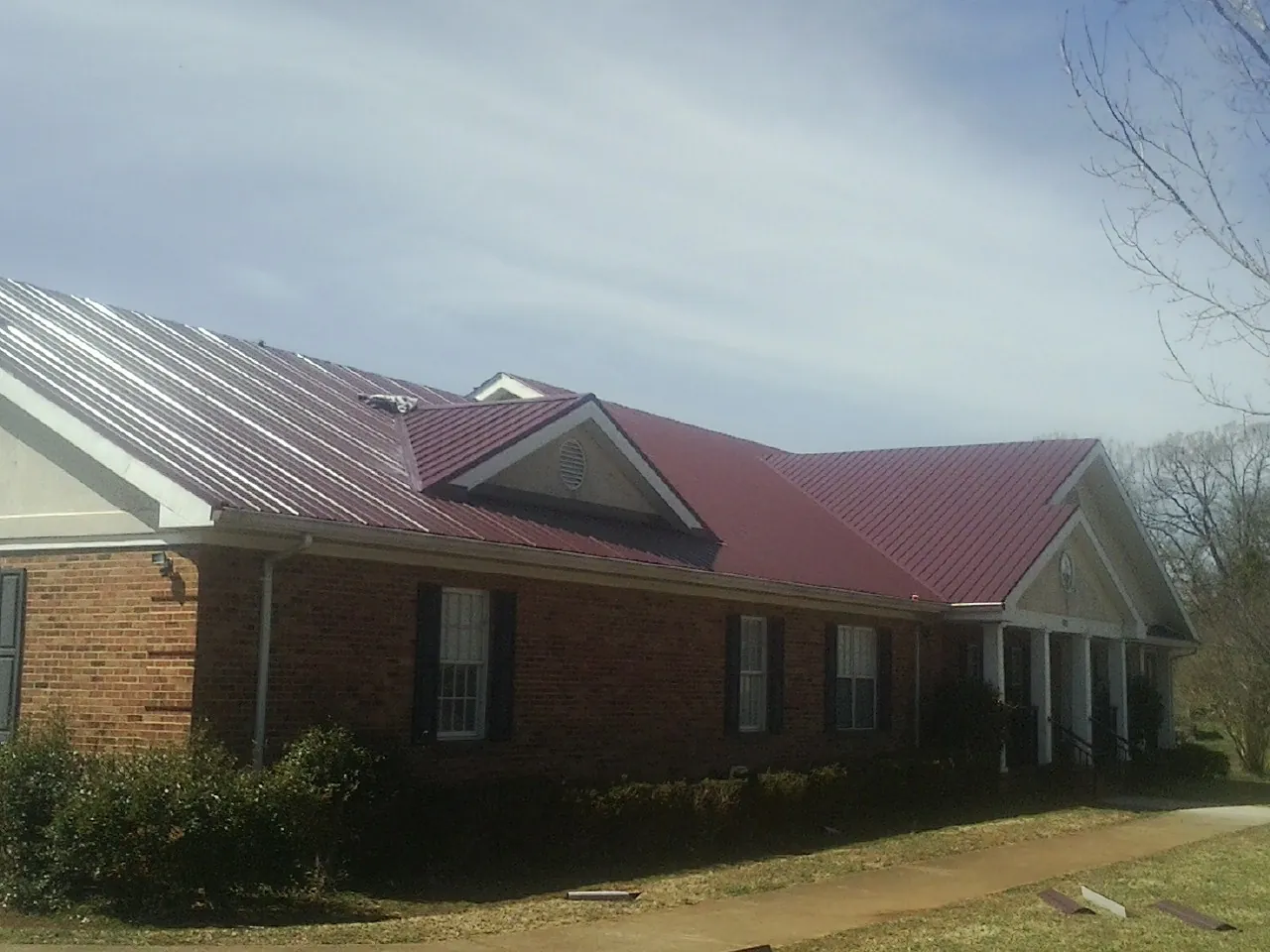 Red metal roof with gabled entries on a long brick building, from a Hail Damage Roof Repair job in Walland