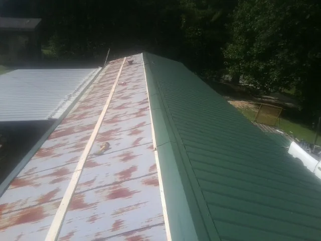 Old rusted panels beside newly installed green metal roofing — Wind Damage Roof Repair by Roofing Brothers in Walland