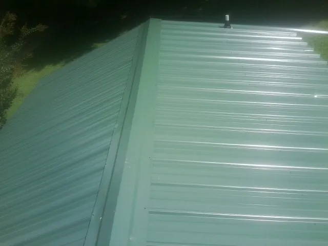 New green metal panels meeting at the ridge of a roof — Flat Roof Repair work by our crew in Walland