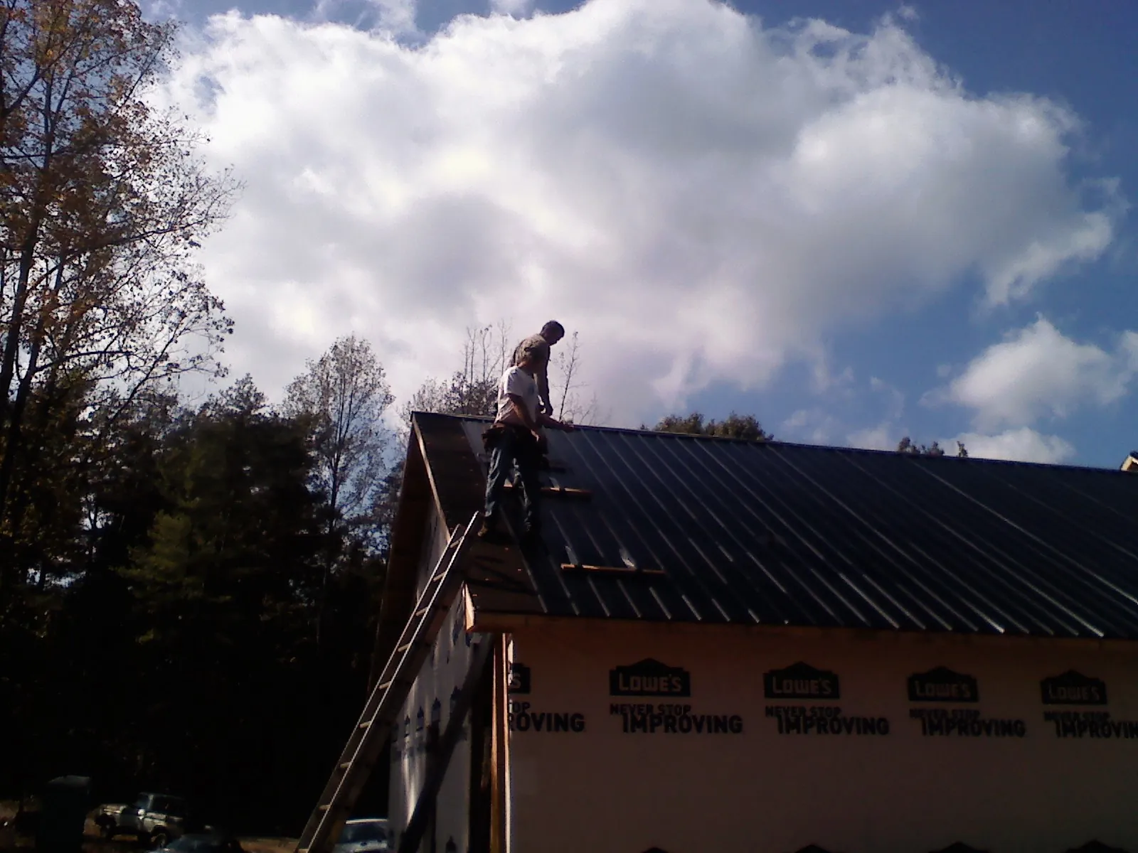 Roofer fastening dark metal panels high against a cloudy sky, from a Roof Inspection job in Walland