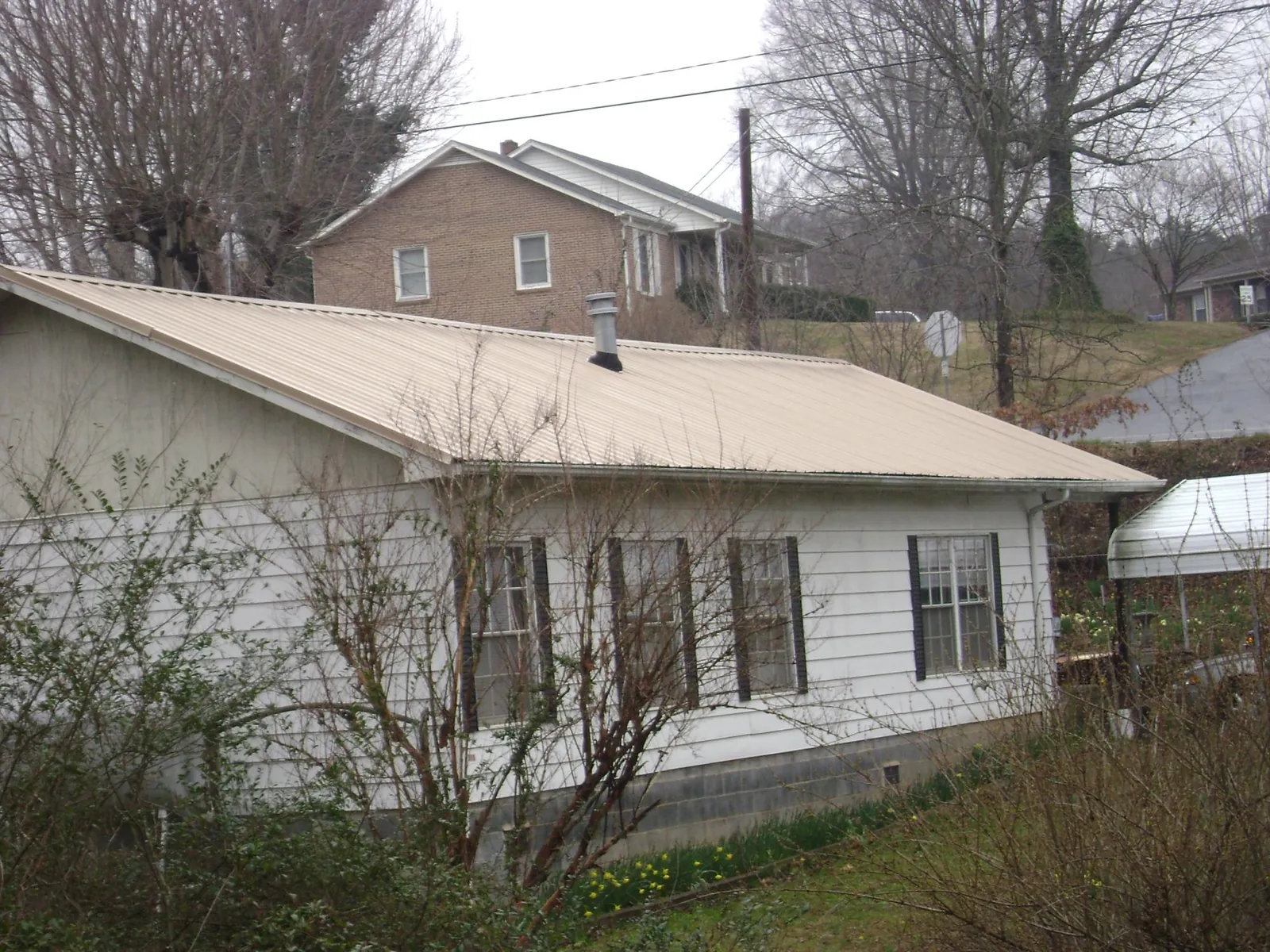 Tan metal roof on a white sided house set into a hillside — Commercial Roofing by Roofing Brothers in Walland